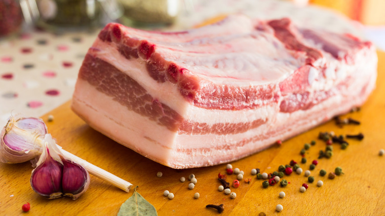 A piece of salt pork on a cutting board beside garlic and pepper cloves