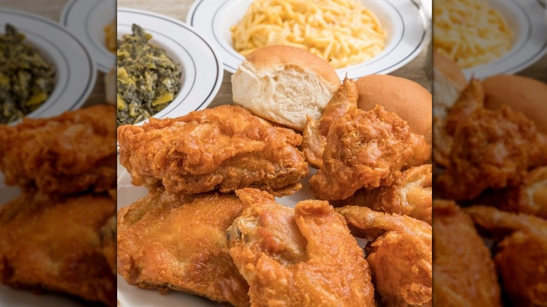 A close-up of a fried chicken plate with greens and mac and cheese in the background