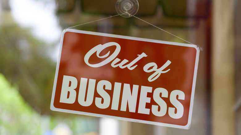 A rectangular red sign with white text that reads "out of business," hanging in the window