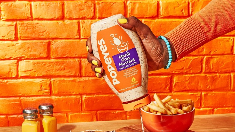 A woman holding a squeeze bottle of Popeyes Louisiana Kitchen Mardi Gras Mustard Dipping Sauce