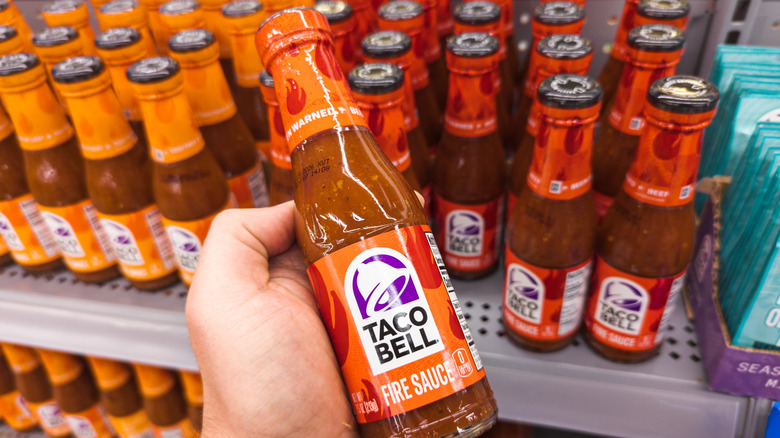 A man holding a bottle of Taco Bell Fire Sauce in a grocery store