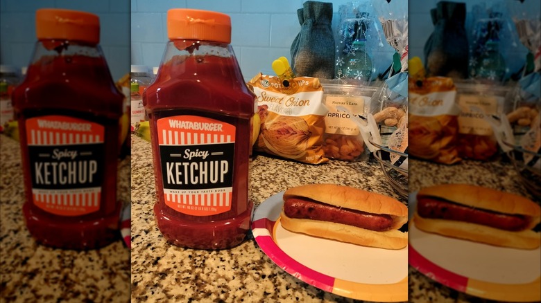 A bottle of Whataburger Spicy Ketchup on a kitchen counter next to a paper plate holding a hot dog