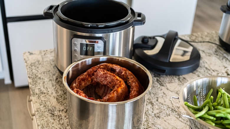 Two racks of ribs rolled up in an Instant Pot on a counter next to a colander of green  beans