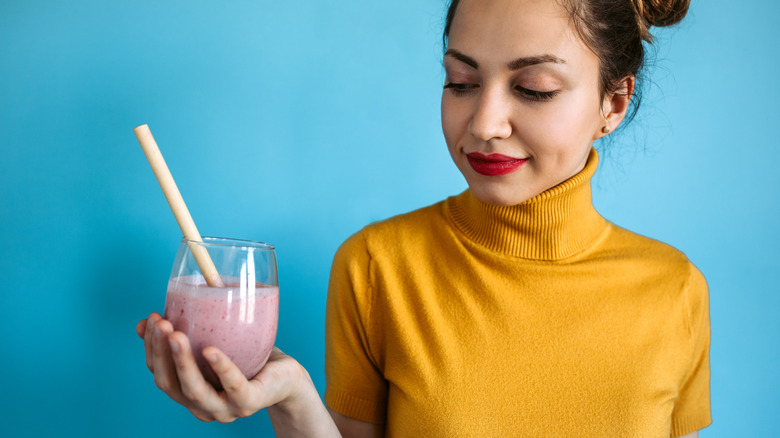 A woman holding a glass filled with a pink smoothie and wide straw