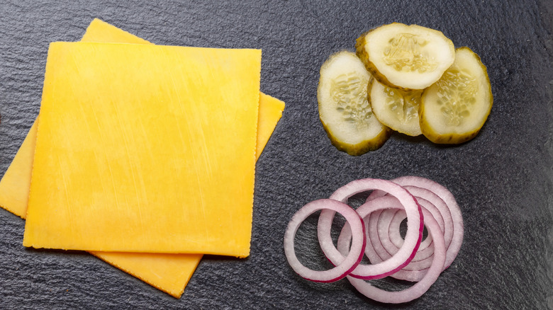 Slices of cheese next to a small stack of pickles and red onion