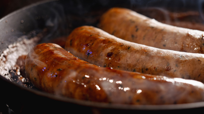 Sausages cooking in a skillet with steam rising from the liquid