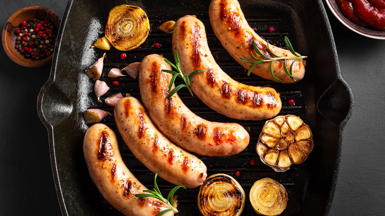 Grilled sausages in a cast iron pan with onions, garlic, and fresh herbs