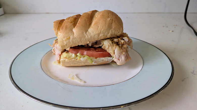 Half of a Jamaican jerk turkey sub on white bread with a tomato and lettuce on a pale plate