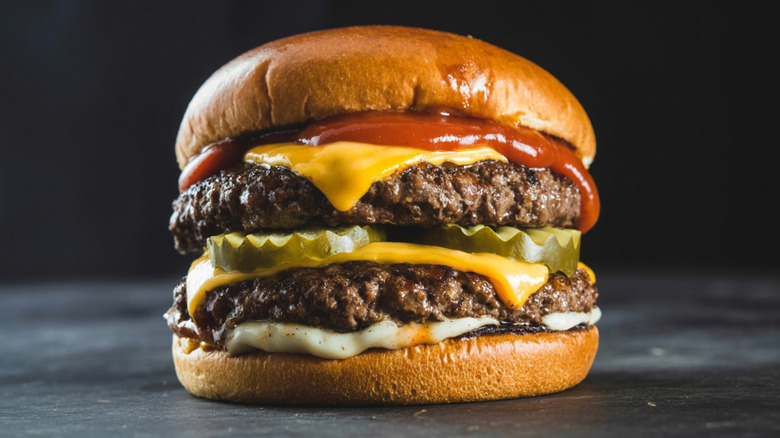 Large hamburger with two beef patties, two slices of cheese, pickles, and ketchup.