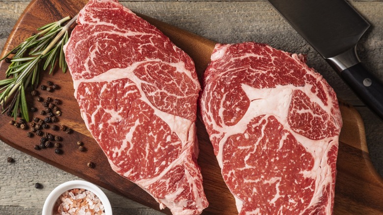 a pair of wagyu steaks on a cutting board next to a knife and thyme