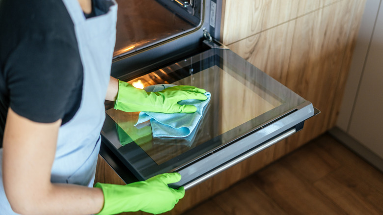 A person wearing green cleaning gloves and wiping down a sparkling clean oven door