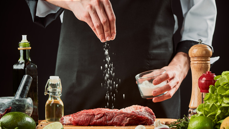 Chef sprinkling salt over meat