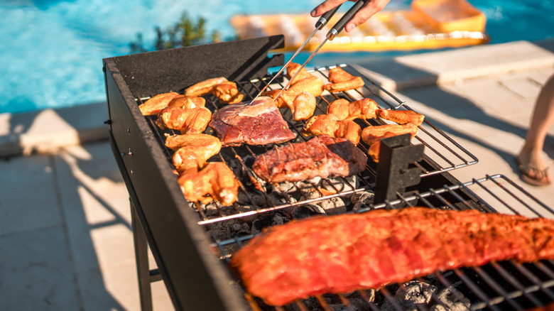 Someone cooking a large amount of chicken wings pork and ribs on flat-top charcoal grill