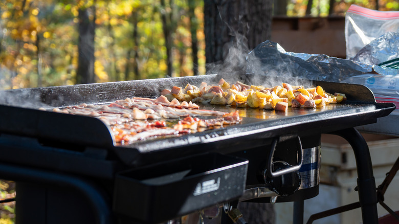 Bacon and potatoes cooking on a flat-top grill