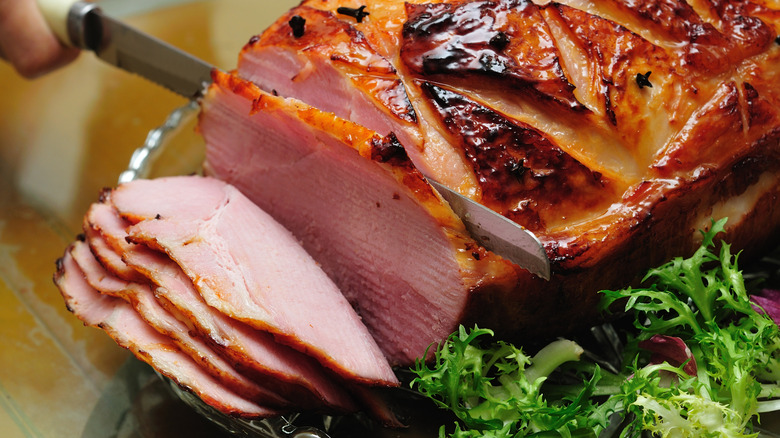 a close up of a person slicing a baked ham