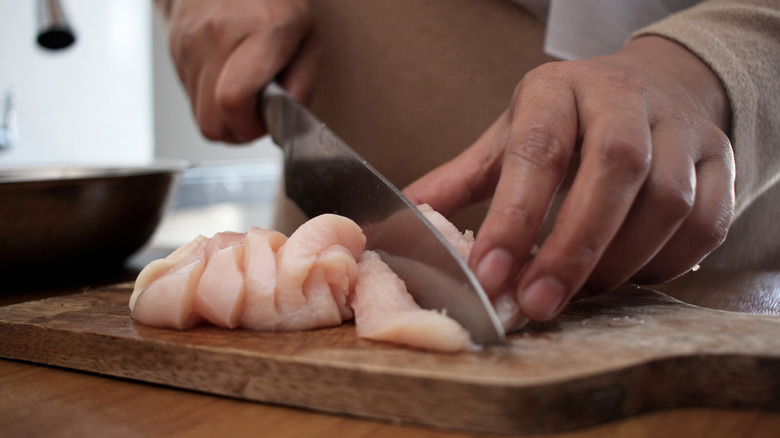 Woman cutting chicken breast