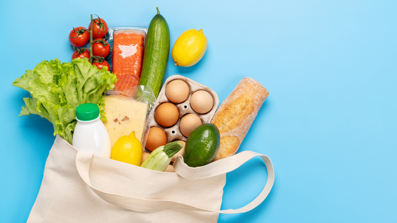 A brown bag of groceries with vegetables, salmon, citruses, eggs, bread, milk, and cheese