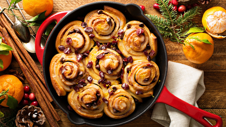 A cast iron skillet packed with freshly baked orange cranberry cinnamon rolls, on a wooden table.