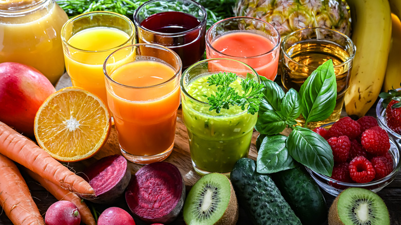row of fruit juices with orange, kiwi, banana, berries, carrots, beets next to cups