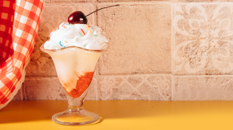 A retro milkshake is garnished with whipped cream and cherry on a kitchen counter.