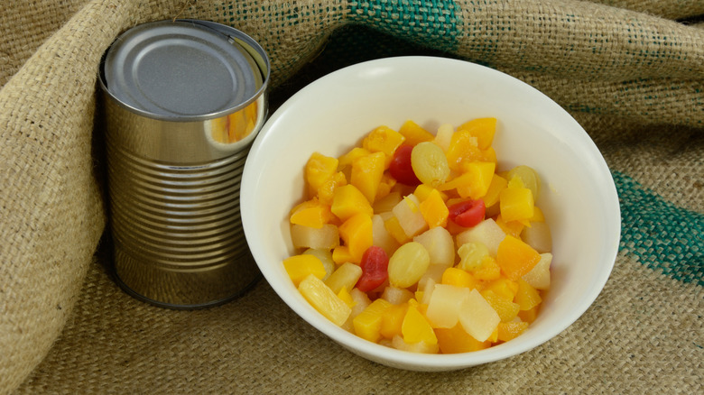 The contents of a can of fruit cocktail are poured into a bowl.