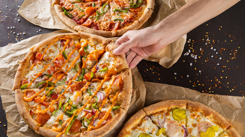 Three pizzas with a hand reaching for a slice