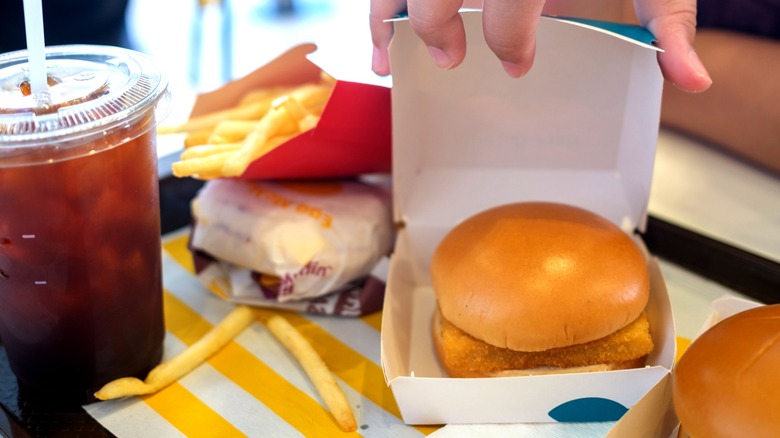 Hand opening cardboard box containing McDonald's Filet-O-Fish sandwich next to cup of soda and french fries