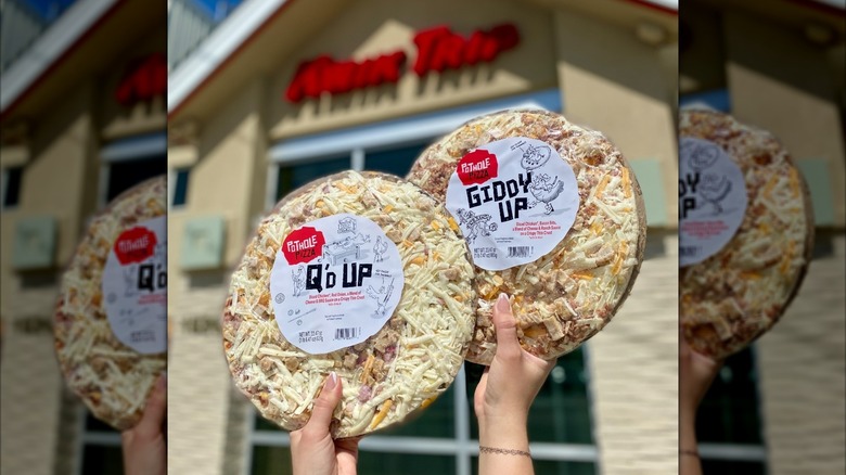 Hands holding up two Pothole frozen pizzas from Kwik Trip in Q'd Up and Giddy Up flavors