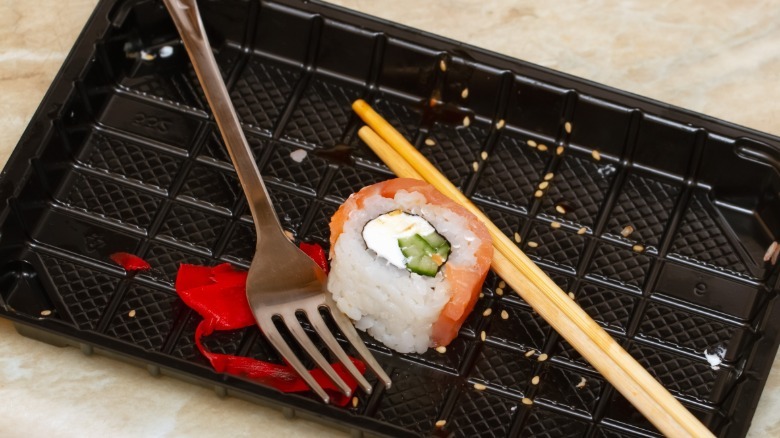 Sushi roll on a black plate next to a fork and chop sticks
