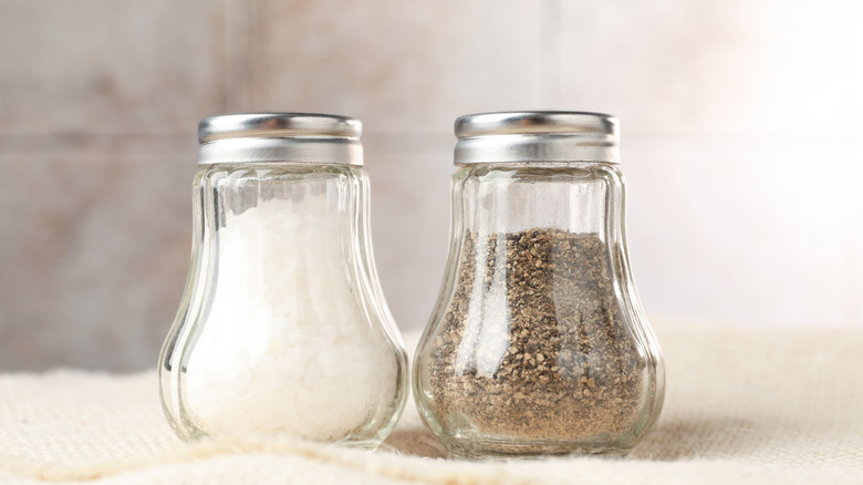 A pair of salt and pepper shakers. They are made of glass and are pear-shaped with aluminum lids