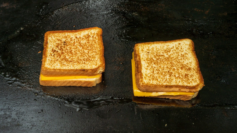 Two grilled cheese sandwiches cooking on an iron griddle