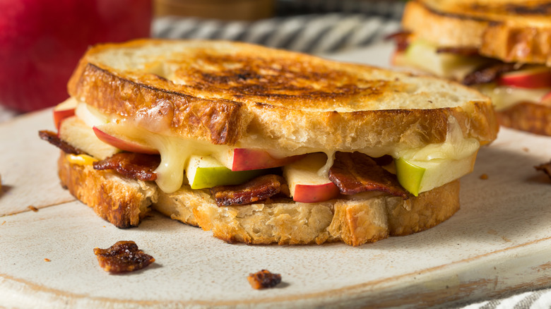 Grilled cheese sandwich filled with apples and bacon on a wooden board