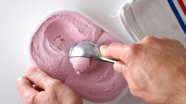 A man scooping ice cream from a tub in his kitchen