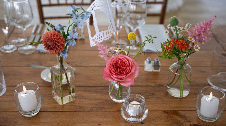 Small floral arrangements in bud vases on a wooden table with candles