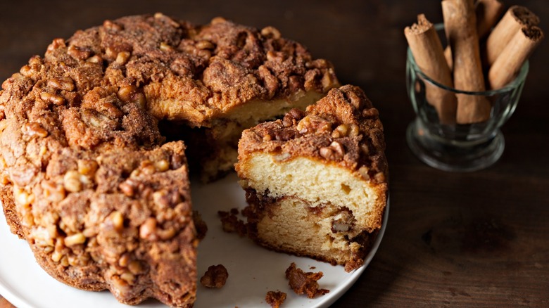 Whole cinnamon coffee cake with one piece cut and cinnamon sticks beside it