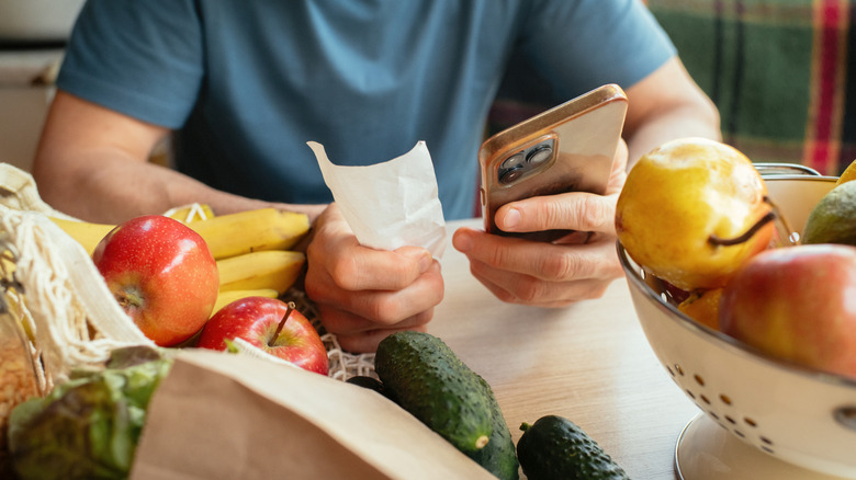 Person holding phone and receipt at table with groceries