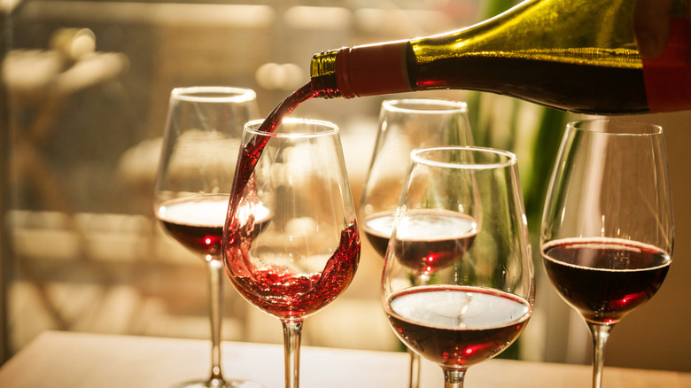 red wine is being poured into various wine glasses on table