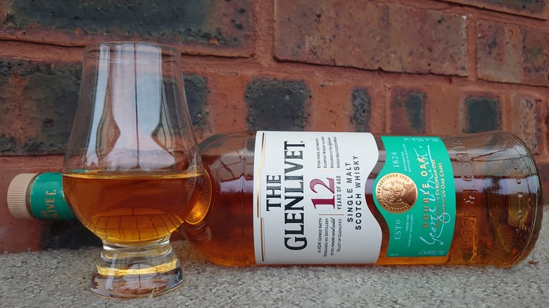 A bottle of The Glenlivet 12-year laid on its side with a filled glass in the foreground