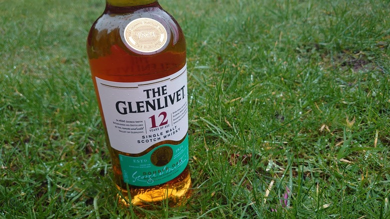 A bottle of The Glenlivet 12-year put up on the grass with spots of rain on the bottle