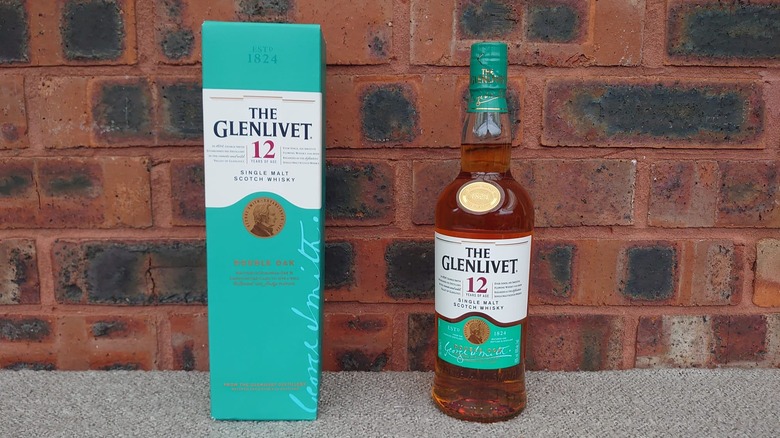 A bottle of The Glenlivet 12-year and its box stood up in front of a red brick wall