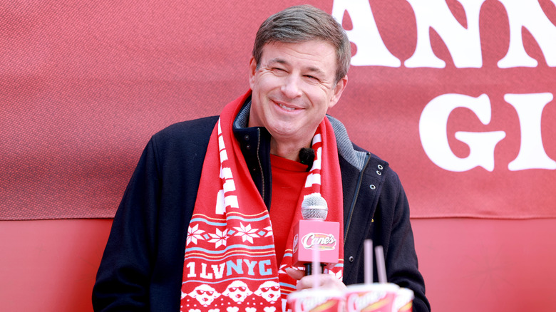 Raising Cane's CEO Todd Graves with a red scarf and black jacket against a red background.