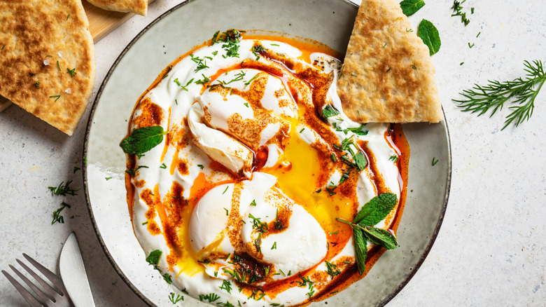 A bowl of creamy, Greek-style poached eggs with herbs, chili oil, and flatbread