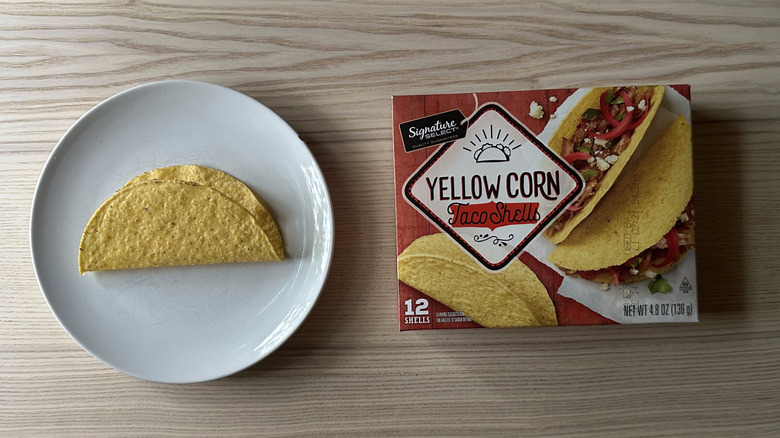A box of Signature Select's Yellow Corn Taco Shells beside one shell on a plate