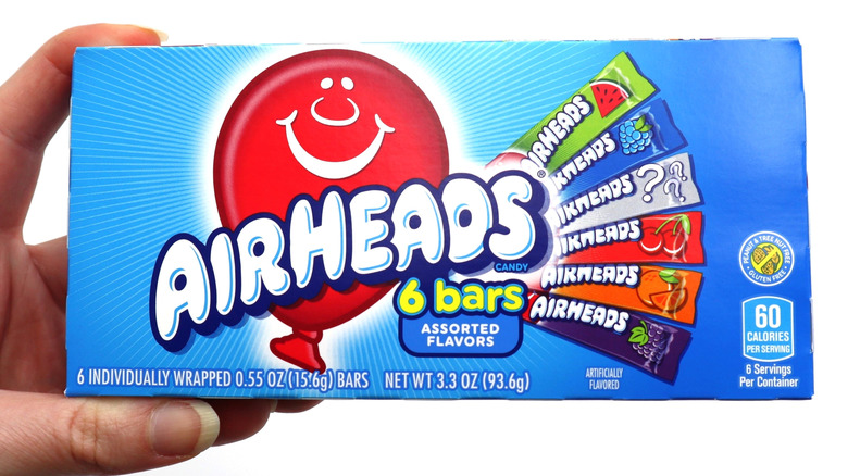 A hand holding up a box of AirHeads candy against a white background