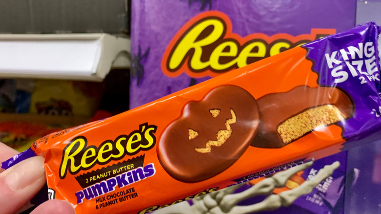 A hand holding up a king-sized pumpkin-shaped Reese's peanut butter candy bar