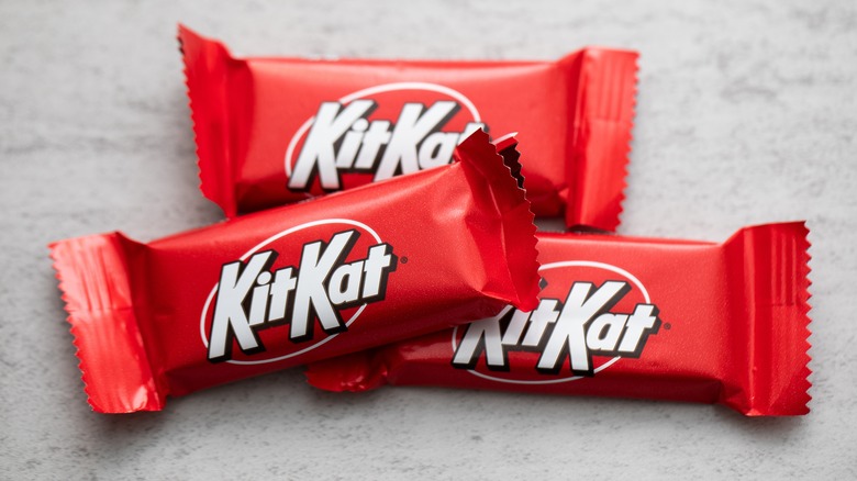 Three individually wrapped mini versions of the KitKat candy bar loosely stacked on a marble countertop