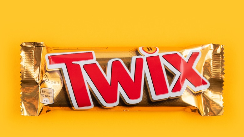A bright yellow background with the gold foil wrapper of a regular-sized Twix candy bar