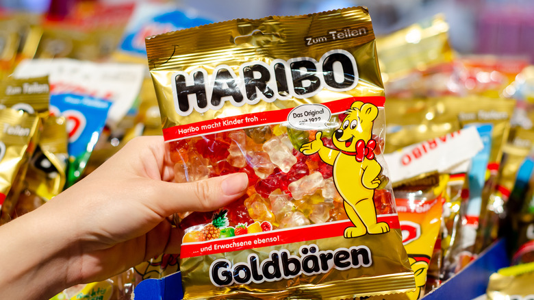 A hand holding up a single bag of Haribo gummy bears in front of a display case