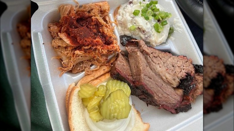 Brisket, pulled pork, rolls, and pickles with salad in a container