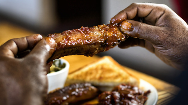 Hands holding a saucy BBQ rib